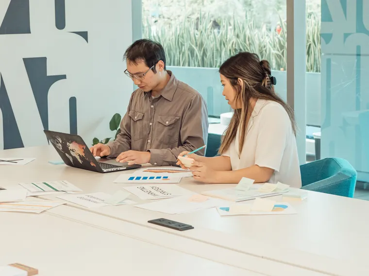Dos colegas colaborando frente a una laptop en una oficina moderna y luminosa durante la jornada laboral